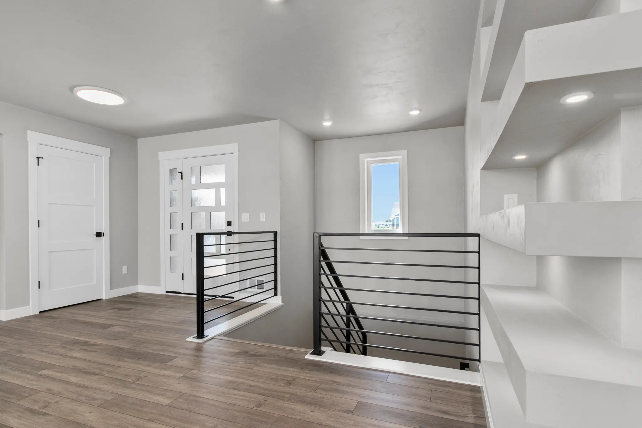 Riverwood entry with a glass-paneled white door, black stair railings, and gray wood-look flooring