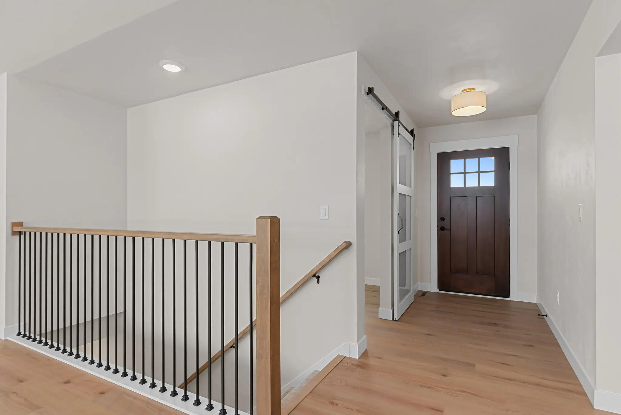 Riverwood entry hall with warm wood flooring, black stair railings, and a barn door