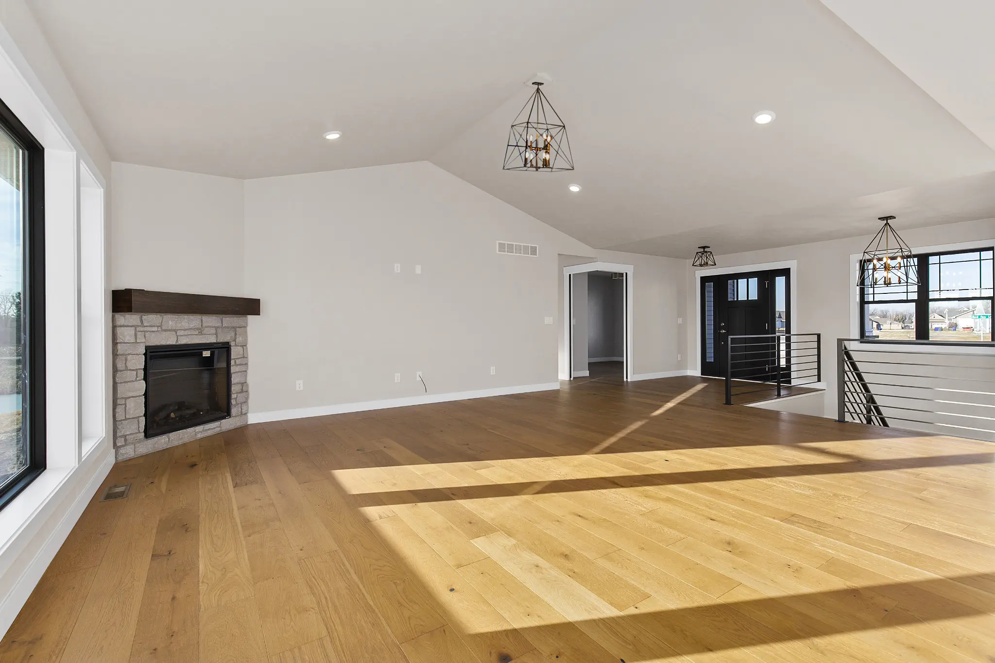 Riverwood vaulted living room with a stone fireplace, black stair railings, and sunlit wood floors